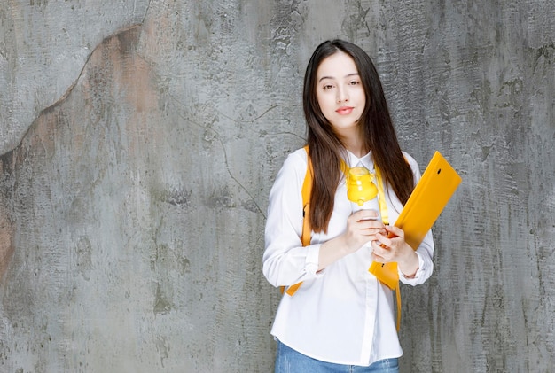 Studentka z żółtym plecakiem trzymając butelkę wody i folder. zdjęcie wysokiej jakości