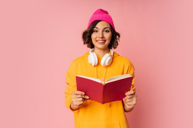 Studio fotografii szczęśliwego słodkiego studenta z notebookami i słuchawkami stojącymi na różowo.