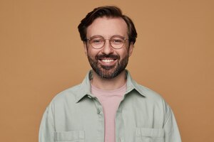 Bezpłatne zdjęcie studio portret brodatego mężczyzny pozowanie na beżowym tle, patrząc w kamerę z szerokim uśmiechem na twarzy