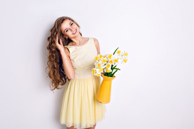 Studio strzał dziewczyny stojącej i trzymając żółty wazon z kwiatami.