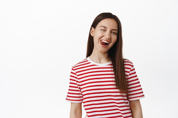 Styl życia ludzi. Portret pięknej dziewczyny mrugając i pokazując język pozytywny, szczęśliwy wyraz twarzy młodej kobiety w swobodnym t-shirt, białe tło. Skopiuj miejsce