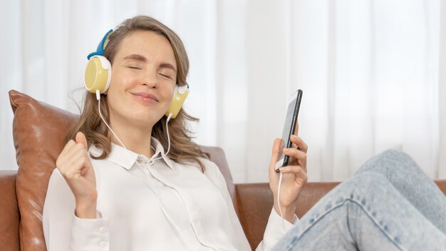 Styl życia Piękna śliczna dziewczyna kobieta czuje się szczęśliwa słuchając muzyki w słuchawkach na kanapie