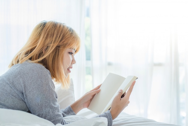 Styl życia szczęśliwa młoda Azjatycka kobieta cieszy się kłamać na łóżkowej czytelniczej książki przyjemności w przypadkowej odzieży