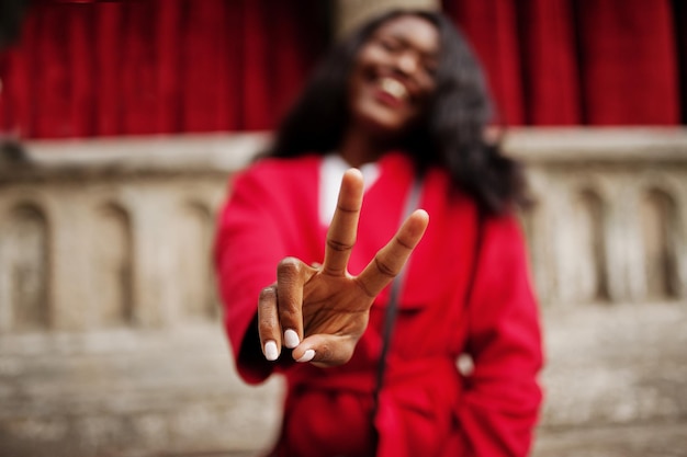 Stylowa Afroamerykanka W Czerwonym Płaszczu Pozuje Na Tle Starych Kolumn I Pokazuje Znak Dwoma Palcami