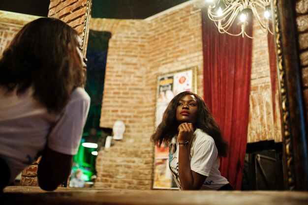 Stylowa afroamerykanka w koszulce z nadrukiem, patrząca w lustro
