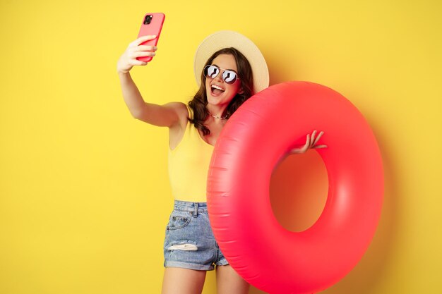 Stylowa brunetka na wakacjach robi selfie z kółkiem pływackim i idzie na plażę pływając w morzu na sum...