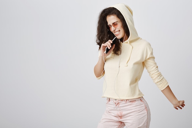 Stylowa dziewczyna grająca w aplikację karaoke, śpiewająca piosenkę w telefonie komórkowym, nosząca słuchawki