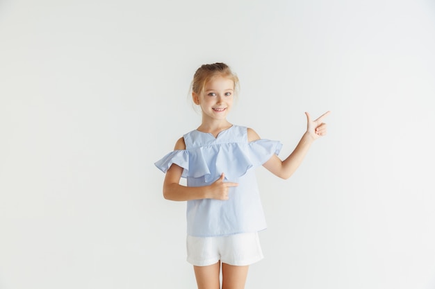Stylowa mała uśmiechnięta dziewczyna pozuje w ubranie na białym tle na białym studio