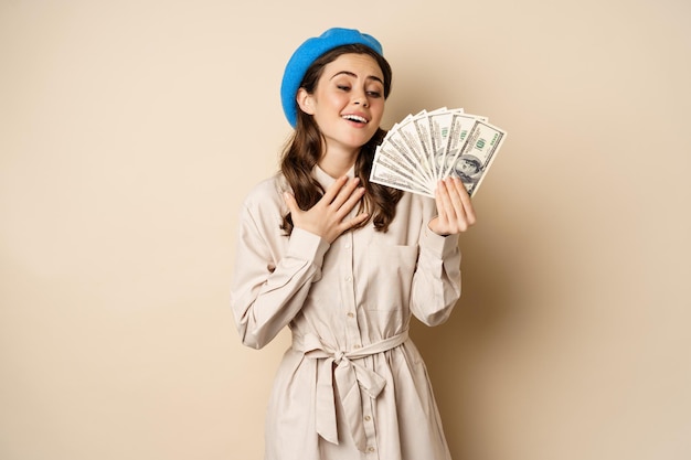 Stylowa młoda kobieta trzymająca pieniądze w gotówce, uśmiechnięta i pozująca, zadowolona, idąc na zakupy...