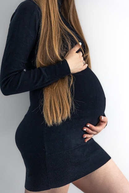 Stylowa młoda kobieta w ciąży w czarnej krótkiej sukience na białym tle