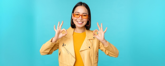 Stylowa piękna Azjatycka kobieta w okularach przeciwsłonecznych, uśmiechnięta zdumiona pokazując znak ok ok, polecająca coś takiego