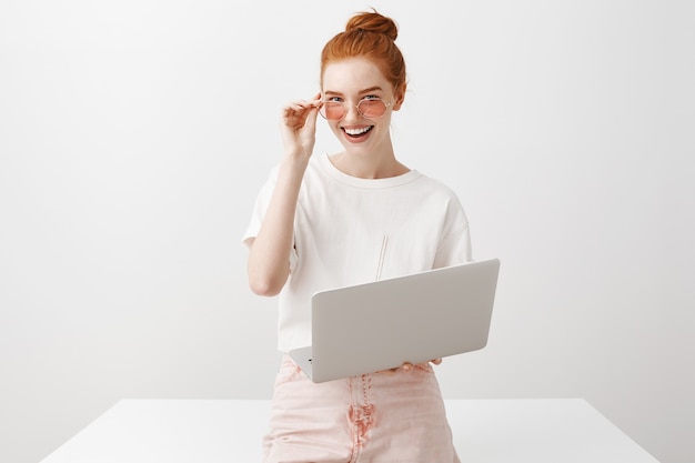 Stylowa ruda kobieta w okularach przeciwsłonecznych do pracy z laptopem