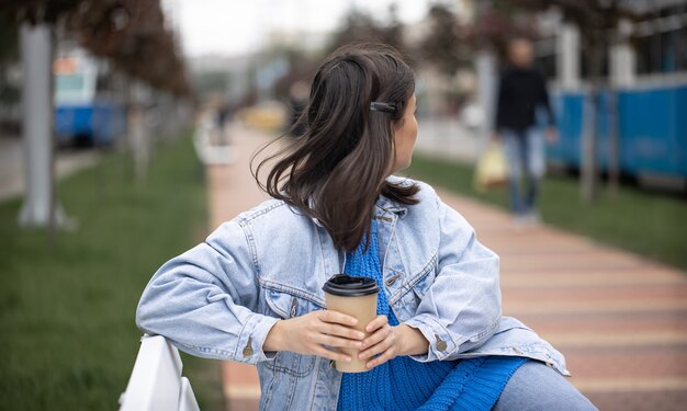 Stylowa wesoła dziewczyna w swobodnym stylu lubi kawę na wynos na spacerze