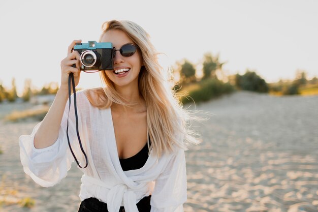 Stylowa zgrabna dziewczyna z aparatem retro, pozowanie na słonecznej plaży. Letni wypoczynek. Tropikalny nastrój. Koncepcja wolności i podróży.
