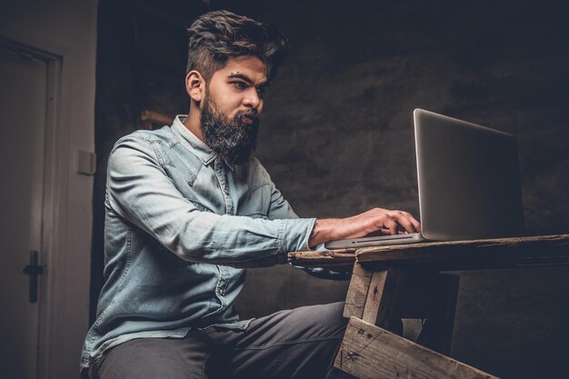 Stylowy brodaty mężczyzna indyjski pracujący z laptopem.