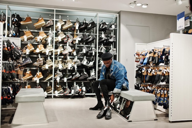 Bezpłatne zdjęcie stylowy dorywczo afroamerykanin w dżinsowej kurtce i czarnym berecie w sklepie z ubraniami, próbujący nowego obuwia