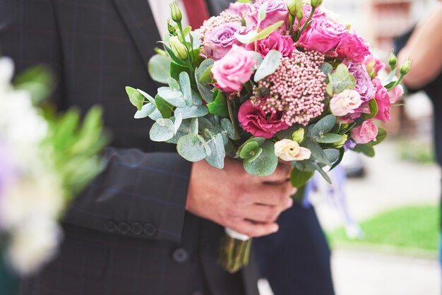 Stylowy pan młody trzyma delikatny różowy bukiet ślubny.