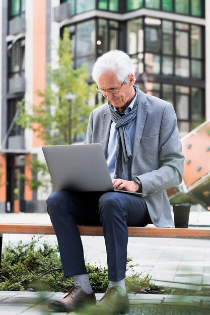 Stylowy starszy mężczyzna w mieście korzystający z laptopa