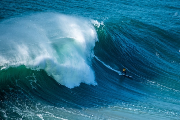 Surfer płynący przez spienione fale Oceanu Atlantyckiego w kierunku wybrzeża Nazare