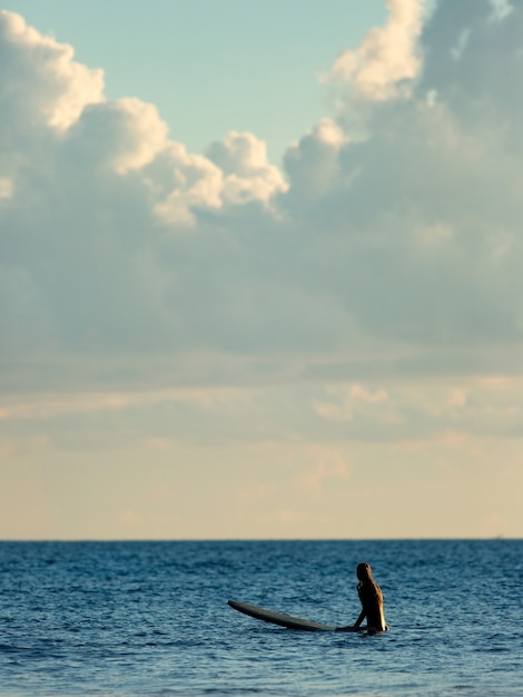 Surfer siedzący w oceanie o zachodzie słońca