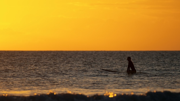 Surfer siedzący w oceanie o zachodzie słońca