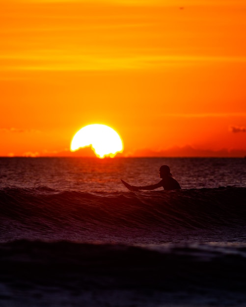 Surfer siedzący w oceanie o zachodzie słońca