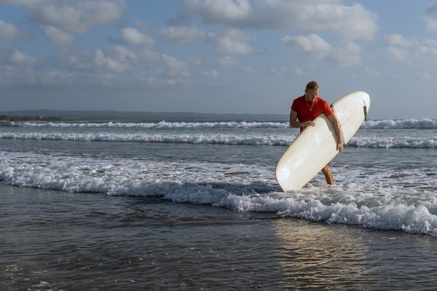 Bezpłatne zdjęcie surfer spacerujący po plaży. bali