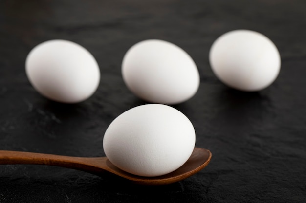Surowe białe jajka i drewniana łyżka na czarnej powierzchni.