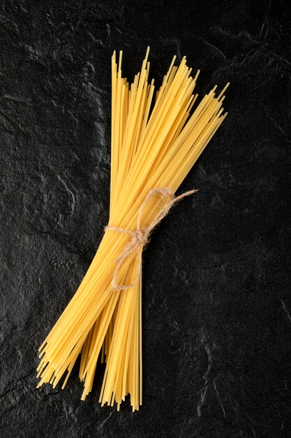 Surowe spaghetti zawiązane sznurem na czarnej powierzchni