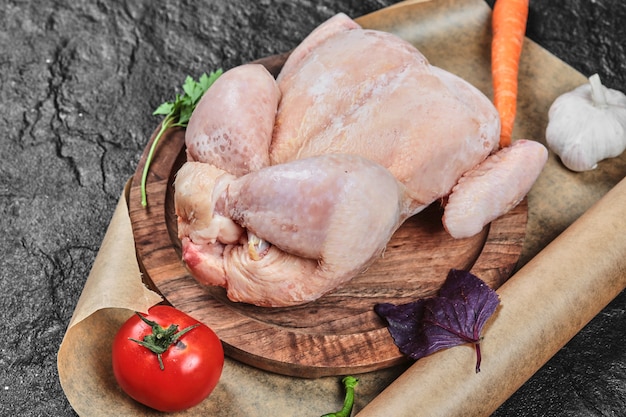 Surowy cały kurczak na drewnianym talerzu ze świeżymi warzywami