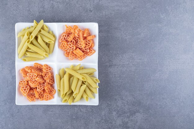 Surowy makaron penne i sercowaty na białym talerzu.