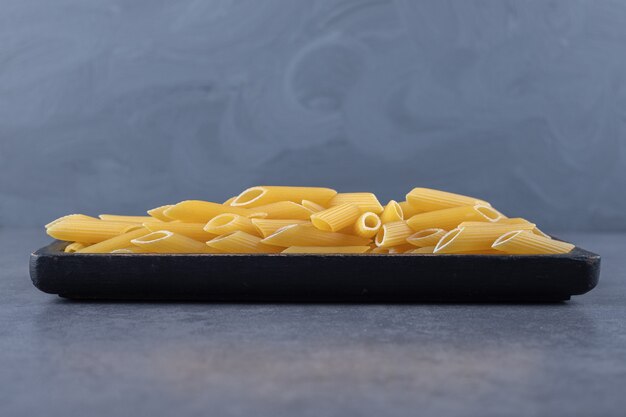 Surowy makaron penne na czarnej płycie.