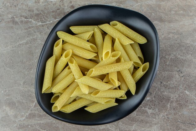 Surowy makaron penne w czarnej misce