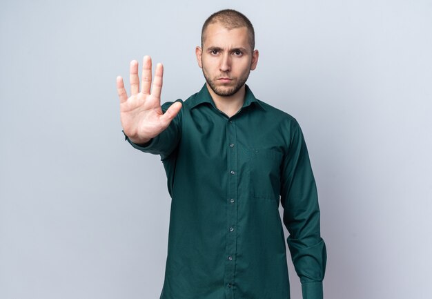 Surowy młody przystojny facet ubrany w zieloną koszulę pokazując gest stop