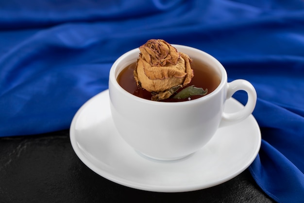 Suszona róża w filiżance gorącej herbaty na czarnym stole.