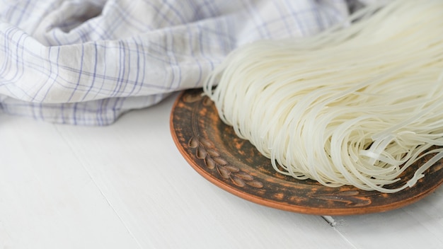 Bezpłatne zdjęcie suszony makaron ryżowy wermiszel na okrągłym talerzu w pobliżu kratkę szmatką na białej powierzchni