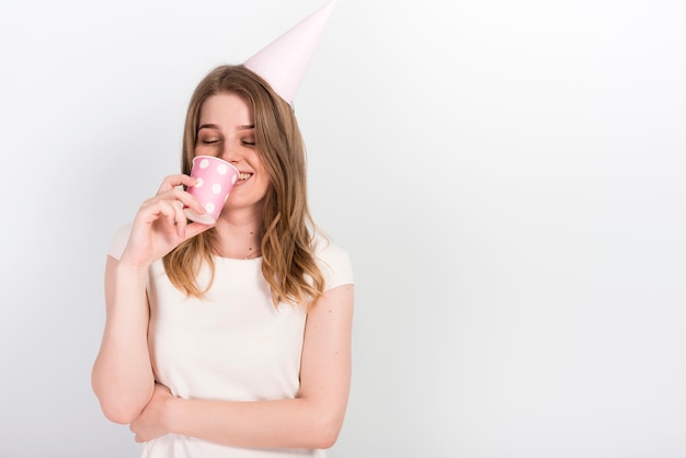 Świąteczna młoda kobieta w partyjnym kapeluszowym pić