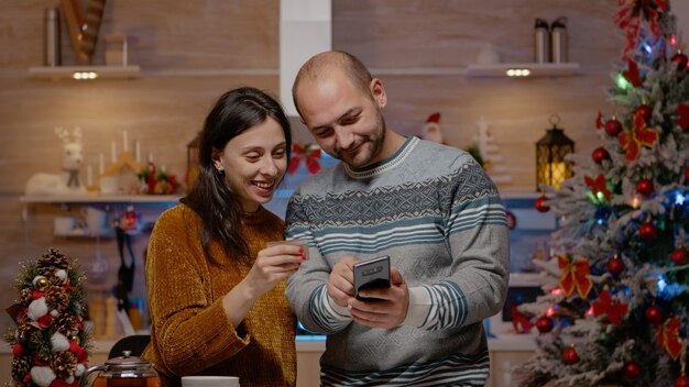 Świąteczna para kupująca prezenty kartą kredytową na smartfonie