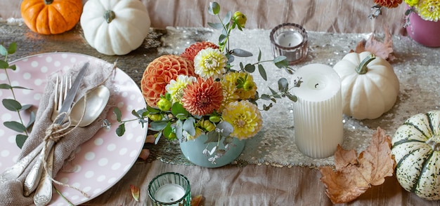 Świąteczne nakrycie stołu ze świecami dyniowymi i kwiatami chryzantem