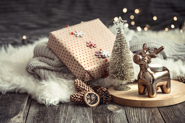 Świąteczne tło świąteczne z zabawkowym jeleniem z pudełkiem na prezent, niewyraźne tło ze złotymi światłami, świąteczne tło na drewnianym stole pokładowym i przytulny sweter na tle