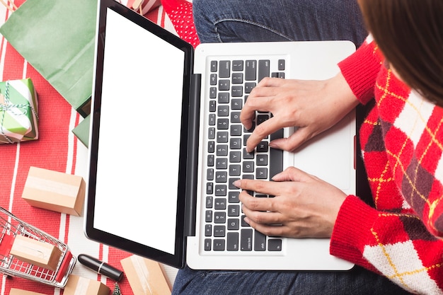 Świąteczne zakupy online. kobieta kupująca z laptopem, przygotowująca się do wigilii, siedząca wśród pudełek i paczek z prezentami. wyprzedaż ferii zimowych