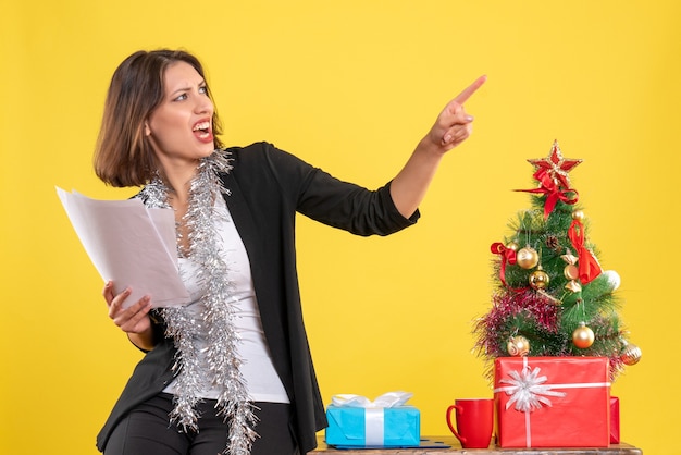 Świąteczny nastrój z emocjonalną nerwową piękną kobietą stojącą w biurze i trzymającą dokumenty w biurze na żółto