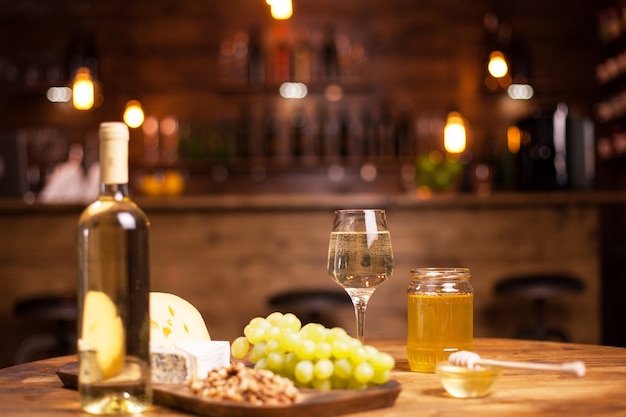 Świetne białe wino na rustykalnym biurku podczas degustacji serów w pubie vintage. Pyszne winogrona. Butelka białego wina. Świeży owoc.
