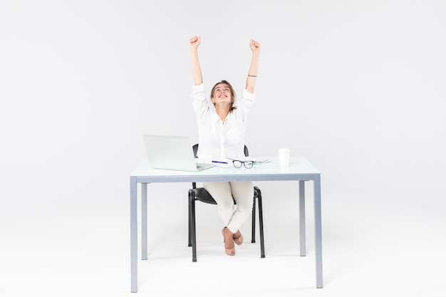 Świętuje bizneswoman przy biurkiem z laptopem odizolowywającym na białym tle