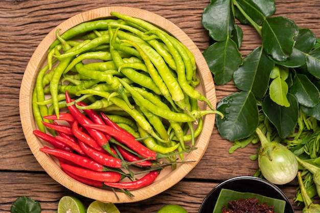 Świeże chili na drewnianej tacy z liśćmi cytryny i limonki kaffir.