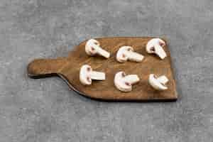 Bezpłatne zdjęcie Świeże pieczarki organiczne plastry na drewnianą deską do krojenia.