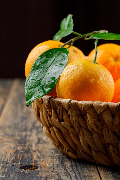 Świeże pomarańcze w wiklinowym koszu z gałęzi widok z boku na czarny i drewniany stół