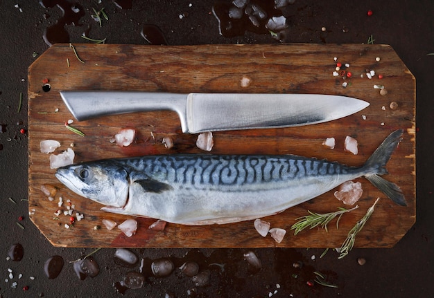 Świeże ryby makreli na desce na czarnym tle. nóż szefa kuchni i organiczne owoce morza w kuchni restauracji. widok z góry, kopia miejsca
