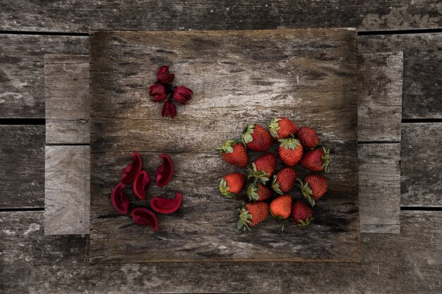 Świeże truskawki i czerwone płatki kwiatów na powierzchni drewnianych