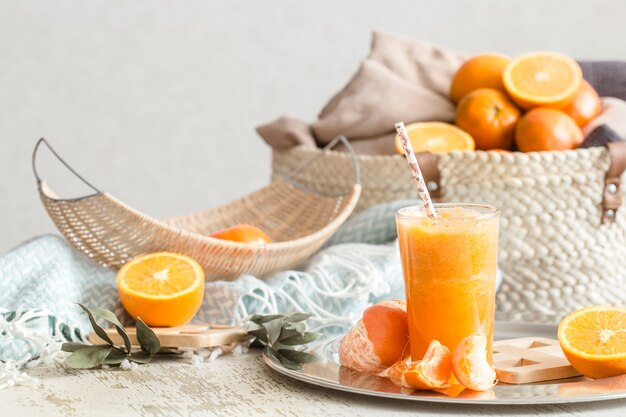 Świeżo uprawiany ekologiczny świeży sok pomarańczowy we wnętrzu domu, turkusowy koc i kosz owoców. Zdrowe jedzenie. Witamina C